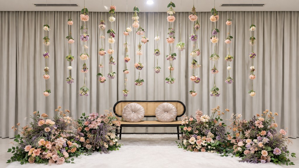 Floral garland mini pelamin with hanging blooms, floor florals and a cane bench on a white rug.