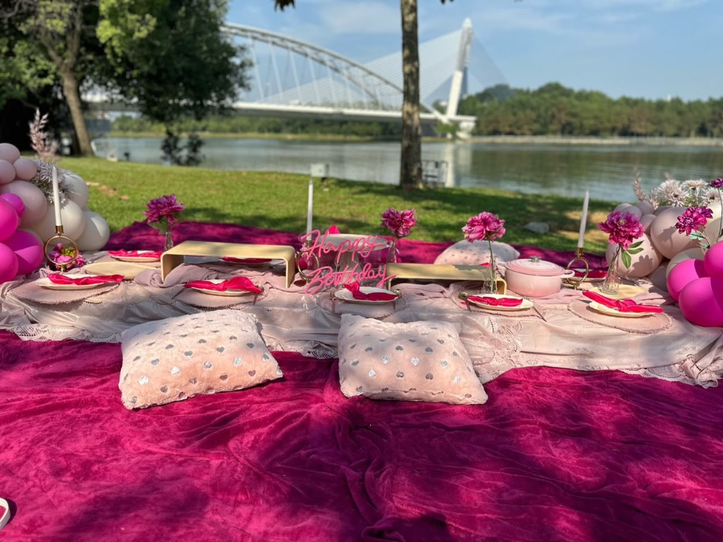 Lakeside picnic styling with a fuchsia blanket, lace runner, Happy Birthday sign, peonies and pink balloon clusters.